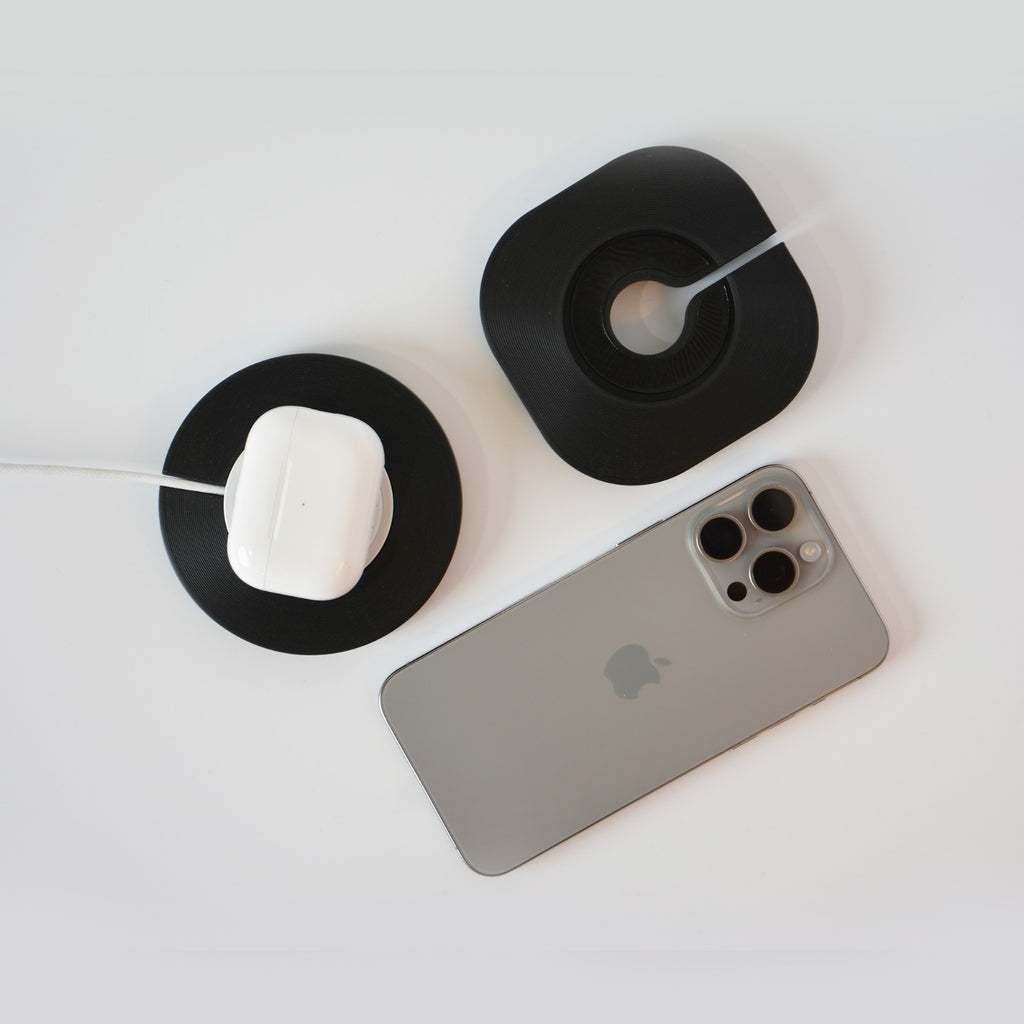 A MagSafe charging dock with a white Apple charger on it and an iPhone placed on the stand. The dock has black and gray colors.